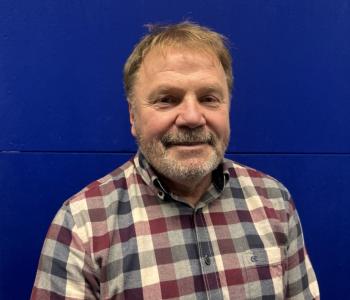 Mann vor blauem Hintergrund. Trägt kariertes Hemd