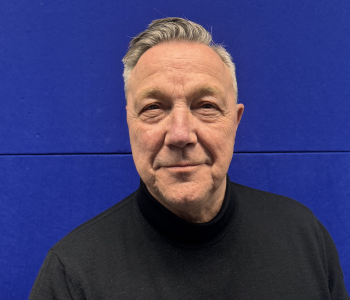 Mann vor blauem Hintergrund. Trägt schwarzen Rollkragenpullover